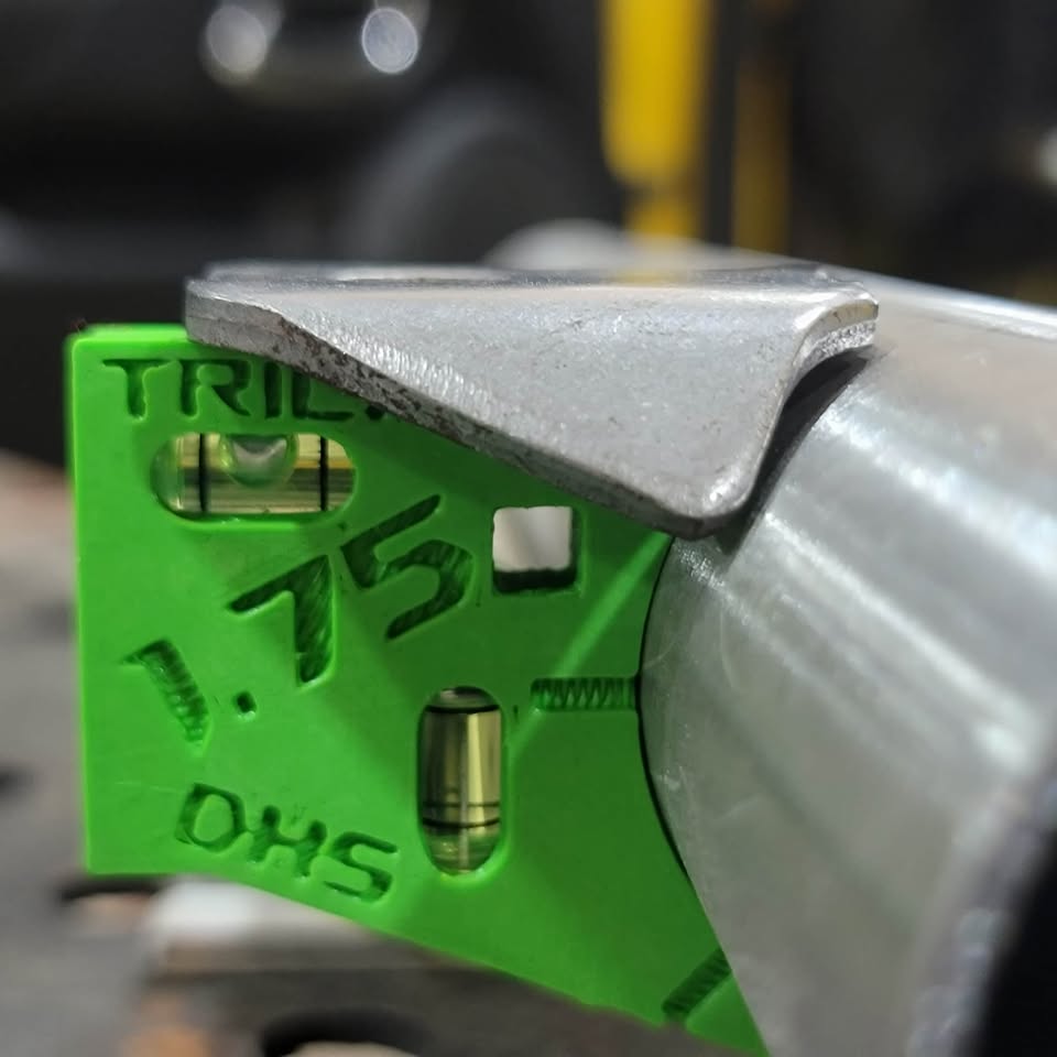 Dead Hand Solutions Chassis Speed Jig clipped onto round tube holding a Trick tab flush, showing the jig in use during chassis fabrication